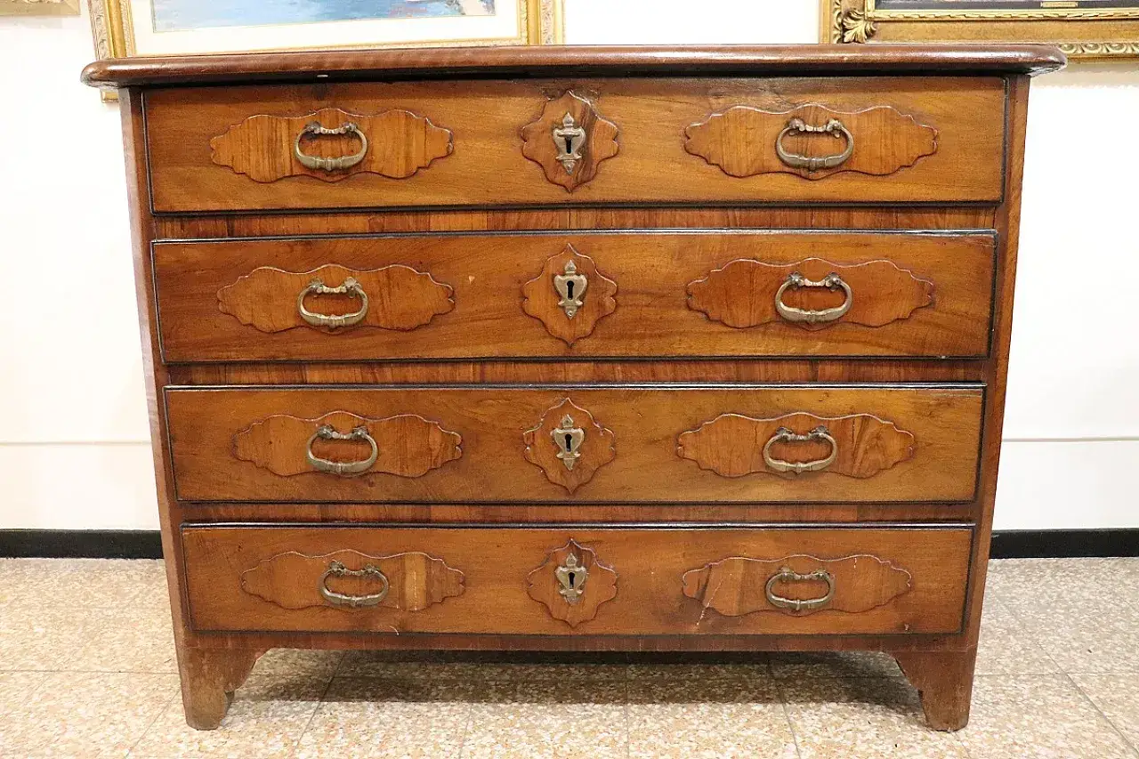 Antico canterano in legno con quattro cassetti, maniglie in ottone e serrature decorative. Un mobile che evoca il significato di storia e artigianalità.