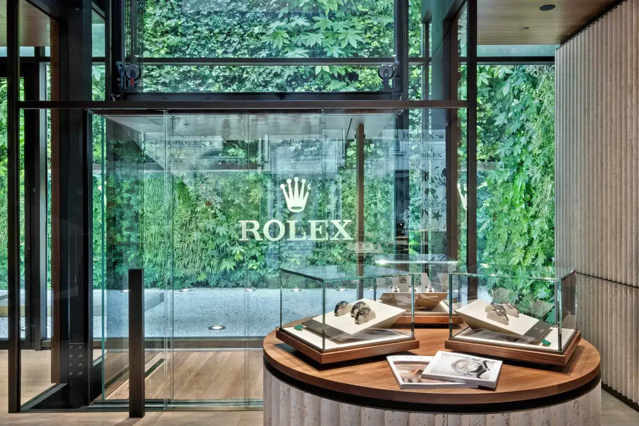 Interno di una boutique Rolex con vetrine espositive di orologi di lusso e una parete verde lussureggiante. La lista attesa Rolex è lunga, ma l'attesa vale la pena.