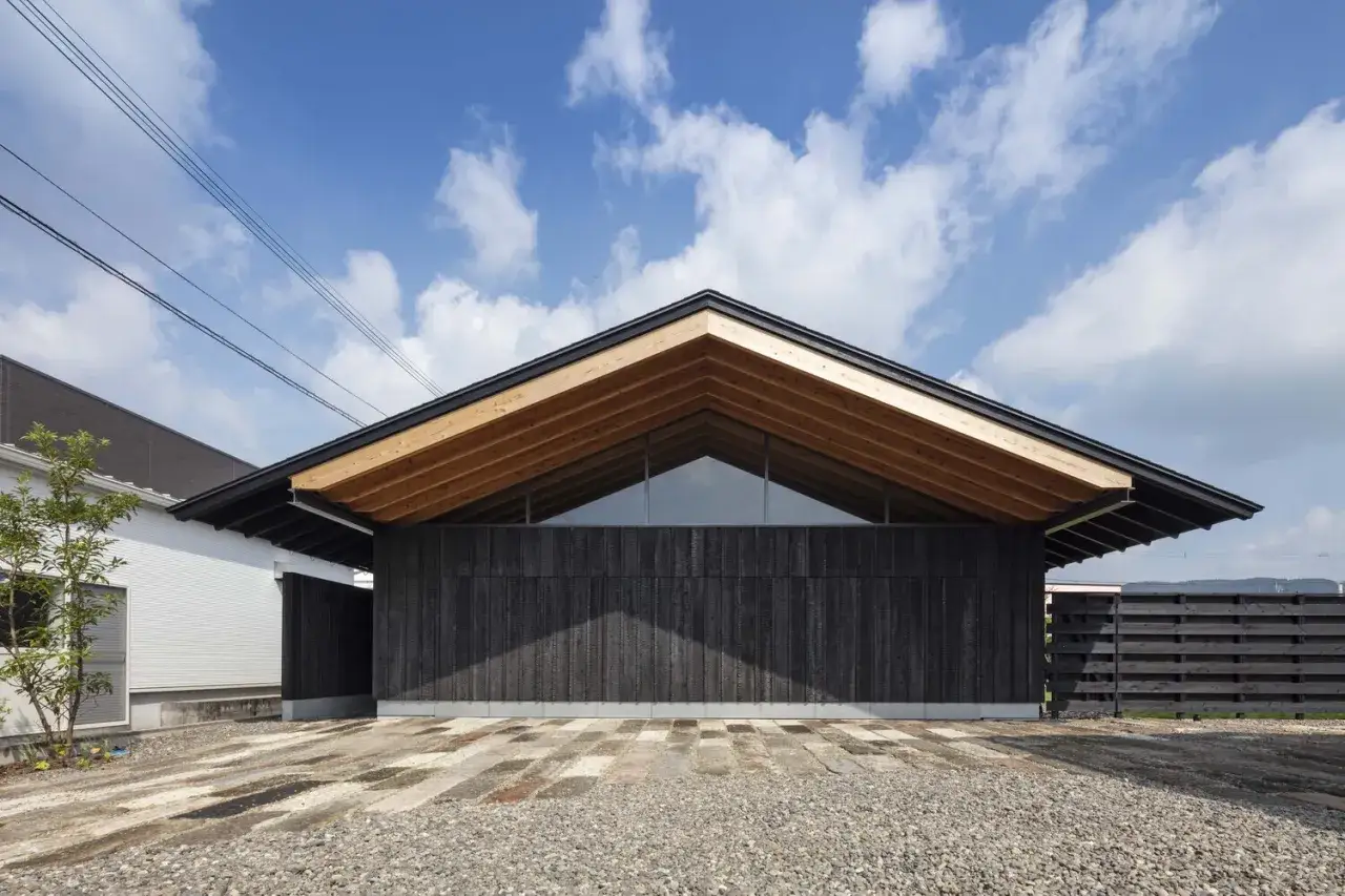 Edificio moderno con facciata in legno bruciato giapponese, tetto spiovente in legno a vista e grande finestra triangolare.
