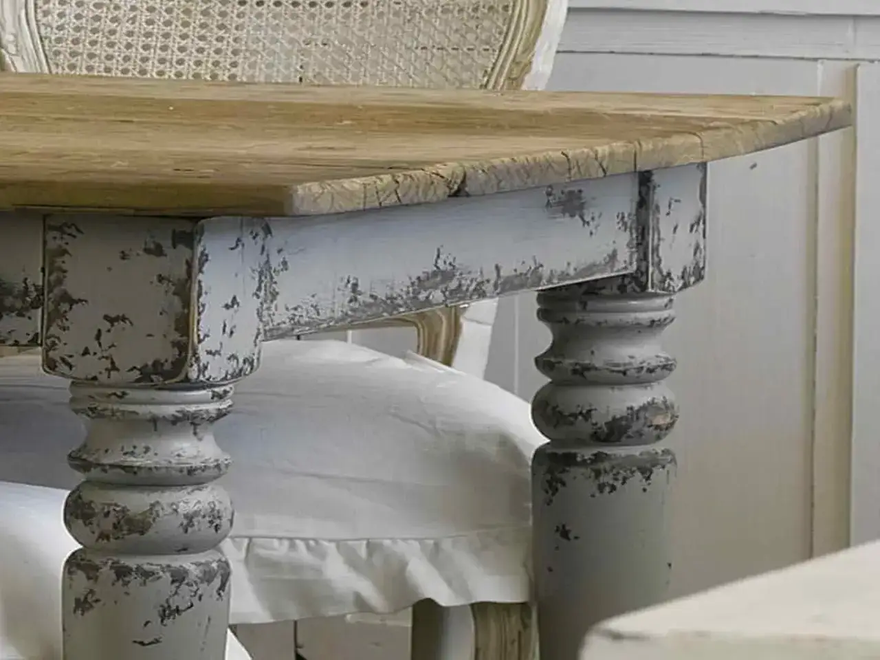 Dettaglio di un tavolo in legno con gambe tornite e vernice grigia scrostata, perfetto per chi vuole imparare come restaurare un mobile antico in stile shabby.