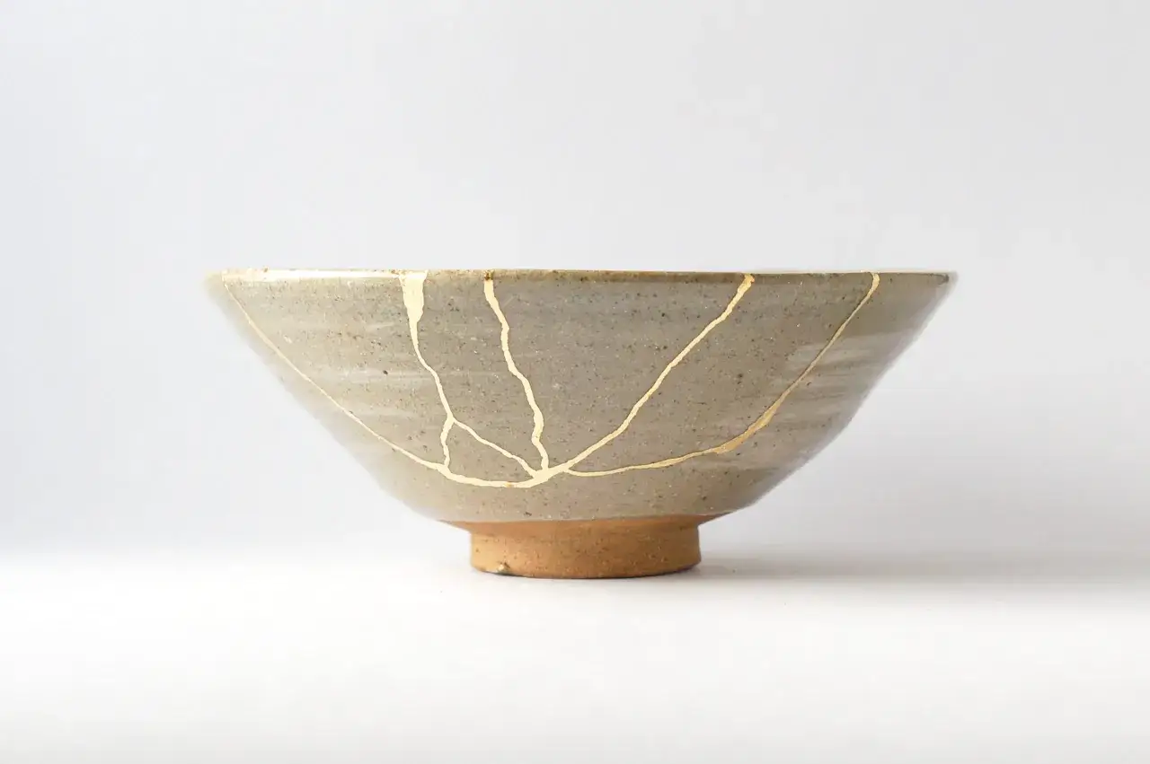 Ciotola in ceramica grigia riparata con la tecnica kintsugi, mostrando come fare per valorizzare le crepe con oro.