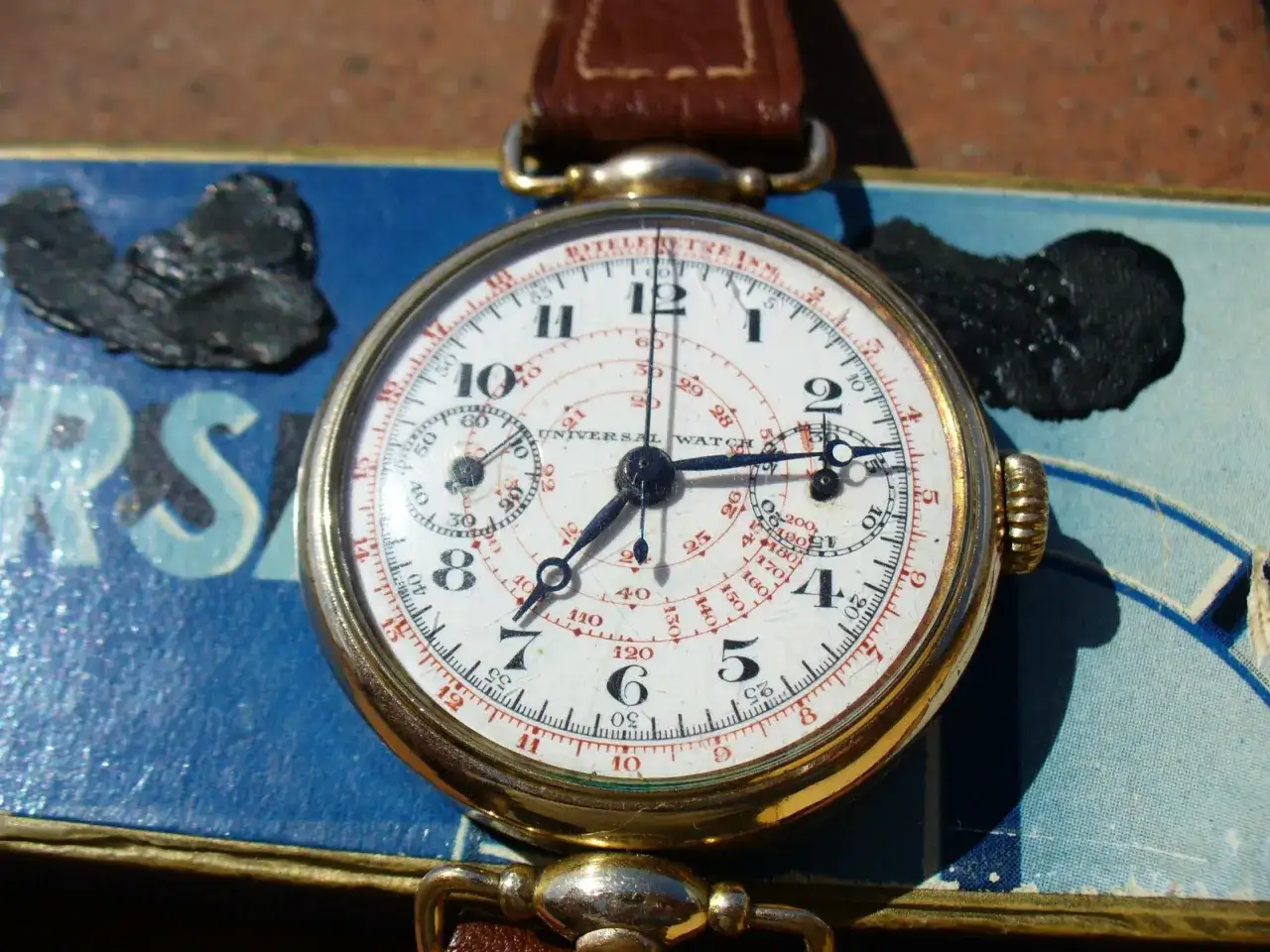 Orologio cronografo Universal Watch con quadrante bianco e indici rossi. Il suo significato è misurare intervalli di tempo con precisione.