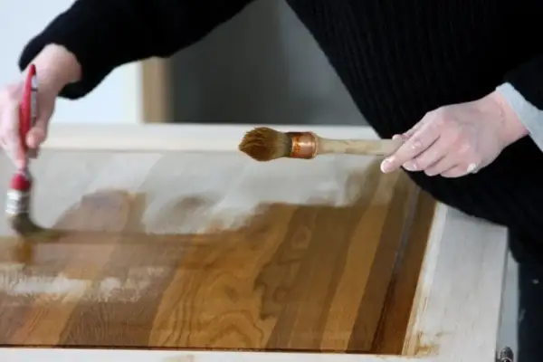 Mani che applicano vernice su un mobile in legno, mostrando come ristrutturare un mobile con cura e precisione.