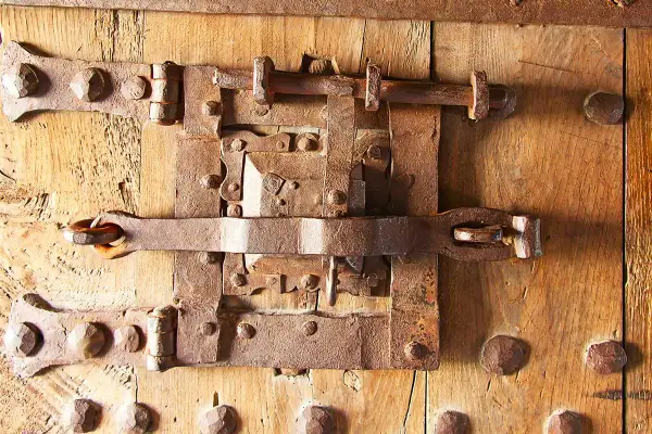Parti di una serratura antica in ferro battuto su una porta di legno. I meccanismi arrugginiti suggeriscono una lunga storia.
