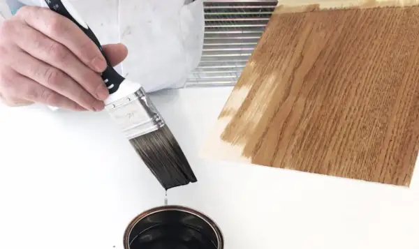 Pennello intinto in latta di impregnante, pronto per applicarlo su un campione di legno.