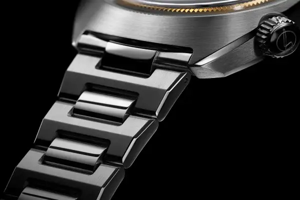 Dettaglio di un orologio con bracciale in metallo spazzolato e lucido. La corona nera presenta un logo inciso, un omaggio a un **singer reimagined**.