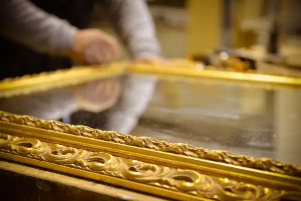 Mani esperte al lavoro per il restauro specchio antico. La cornice dorata e intarsiata riflette la cura del dettaglio.
