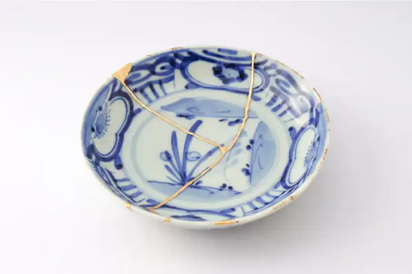 Piatto blu e bianco con crepe dorate, un esempio di tecnica del kintsugi che celebra la bellezza delle imperfezioni.