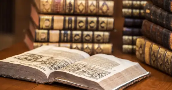 Un antico libro aperto mostra incisioni dettagliate, circondato da pile di volumi rilegati in pelle, testimoni di preziosi libri costosi.