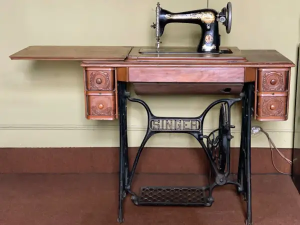 Macchina da cucire Singer d'epoca, con piano in legno e cassetti intagliati. Il suo valore storico la rende un pezzo da collezione.