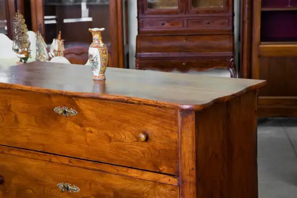 Cassettiera in legno con maniglie antiche e vaso decorato. Un esempio di come antichizzare un mobile per un tocco vintage.