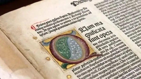 Dettaglio di antichi **primi libri stampati** con iniziale miniata e testo in latino.