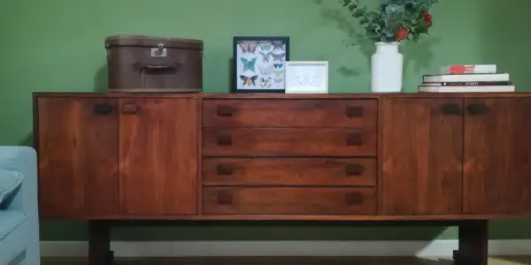 Mobile in legno scuro con cassetti e ante, decorato con una valigia vintage, quadri di farfalle e un vaso di fiori. Un esempio di restyling mobili che unisce passato e presente.