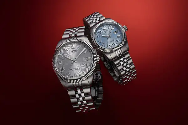 Due orologi Tissot con quadrante argentato e blu, entrambi con movimento automatico Powermatic 80, su sfondo rosso.