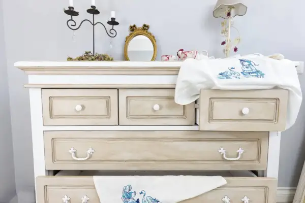 Comò in stile Chippendale rinnovato con finitura anticata. Cassetti con maniglie decorative e un ricamo di cigni su un cassetto aperto.
