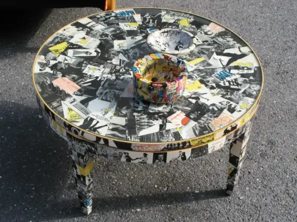 Tavolino rotondo con tecnica decoupage mobili, ricoperto di immagini in bianco e nero e fumetti colorati.